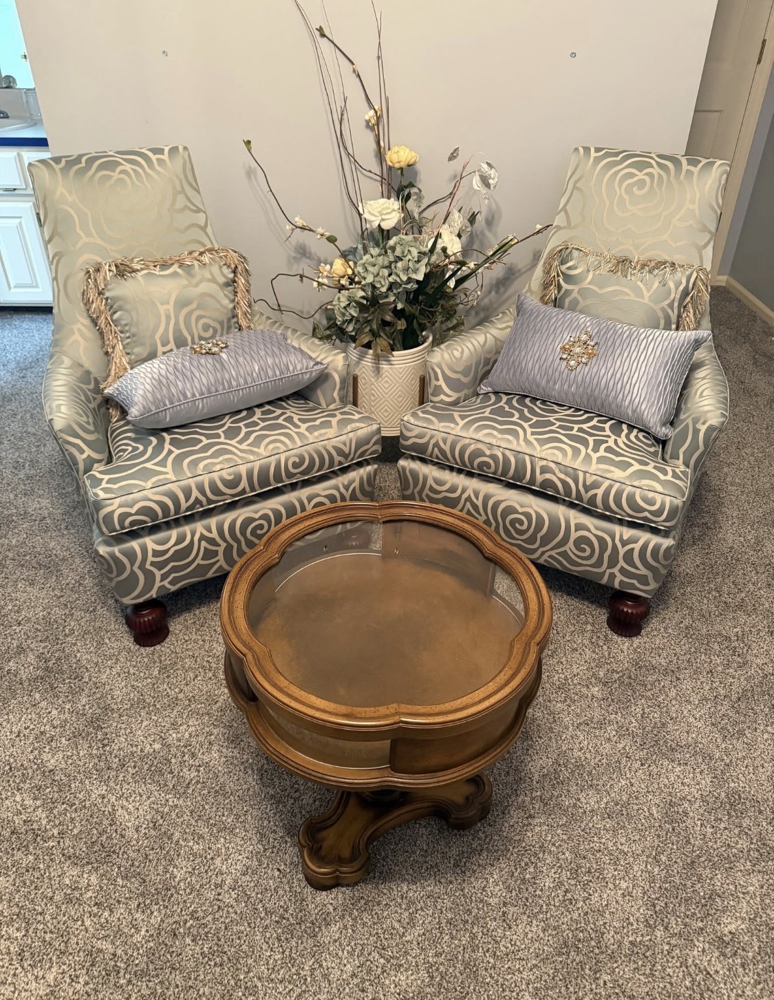 Cozy seating area with two patterned chairs, accented with decorative pillows, and a wooden table, surrounded by a floral arrangement.